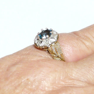 ovales Einzelstück, Blautopasring aus 375 Gold, eine ovale Rosette aus 8 Herzen mit je einem Diamant im Pavé gefaßt, in den Tiefen rhodiniert, ein ovaler, facettierter, aquamarin-hellblauer Edeltopas mit 8 Krappen gehalten, floral gravierte Seitenflächen / Seitenteile & poliert, Ringweite 57 - Goldschmiede Danilo