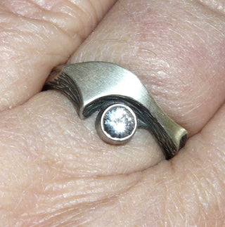Einzelstück, Nordform-Design, Nordform-Ring "großer Schweif" aus 925 Silber mit einem runden, funkelnd facettierten Bergkristall, seidenmatt, in den Tiefen geschwärzt, verstellbare Ringweite bis ca. 62. Anlaufgeschützt. Die gesamte skandinavische / finnische Nordform-Kollektion ist so designt, daß fast alle Schmuckstücke miteinander kombinierbar sind. Besonders gut zu diesem Schmuckstück paßt der Anhänger Nord 0018 + den Ohrringen Nord 0065, 0066 -	Finnlandschmuck bei Goldschmiede Danilo