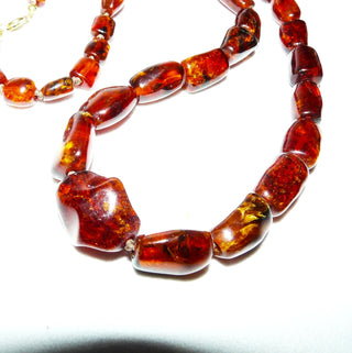 antikes Einzelstück, handgearbeitete Vintage-Bernstein-Kette aus polierten größeren Tönnchen im Verlauf mit einem Mittelstein, durchgeknotet, dunkleres Rotbraun mit schönen Einschlüssen, Verschluß aus Gold-Doublé, Gesamtlänge 60 cm, um 1950 -	Unikatschmuck nur erhältlich im Onlineshop von Juwelier & Goldschmiede Danilo! 