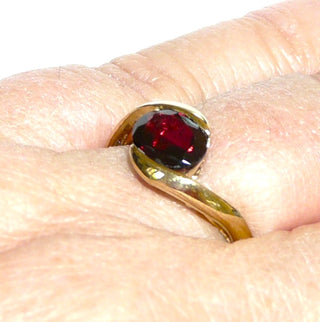 Vintage-Einzelstück, Granatring aus 333 Gold mit einem ovalen, funkelnd facettierten Almandin-Granat mit natürlichen Einschlüssen, ein hochgezogenes schlichtes Oberteil mit einer geschwungenen Schiene, deren Enden den Stein von 2 Seiten umschließt, Ringweite 60,5, um 1975 - Goldschmiede Danilo