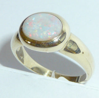 Einzelstück, breiter Ring aus massivem 585 Gelbgold mit einem weißen, kristallinen, australischen Opal-Cabochon. Das schillernde Oval ist interessant quer zum Finger eingearbeitet, der große Stein schillert herrlich in allen Farben, aber mit besonders viel Rot Der Ring ist poliert und der Stein sicher in einer breiten Zargenfassung eingefaßt, Ringweite 59 -	Unikate und Pretiosen nur erhältlich im Onlineshop der Goldschmiede Danilo!