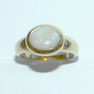 Einzelstück, breiter Ring aus massivem 585 Gelbgold mit einem weißen, kristallinen, australischen Opal-Cabochon. Das schillernde Oval ist interessant quer zum Finger eingearbeitet, der große Stein schillert herrlich in allen Farben, aber mit besonders viel Rot Der Ring ist poliert und der Stein sicher in einer breiten Zargenfassung eingefaßt, Ringweite 59 -	Unikate und Pretiosen nur erhältlich im Onlineshop der Goldschmiede Danilo!